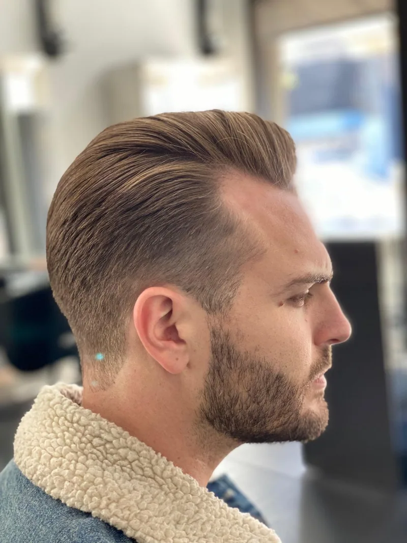 Zijaanzicht van een man met gefade zijkanten, een naar achteren gekamd kapsel en een volle baard