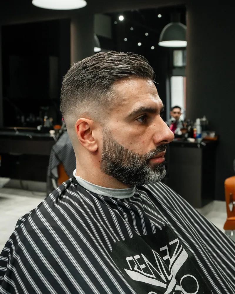 Man in de kappersstoel met een kort geknipt kapsel met fade en een volle baard